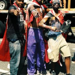Three men in red capes pointing at camera
