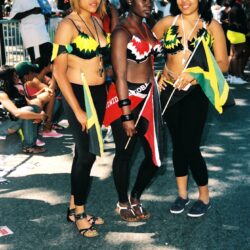 Three women in colorful carnival outfits holding flags