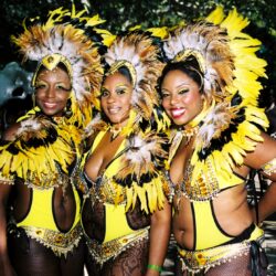 Three smiling women in yellow feathered carnival costumes