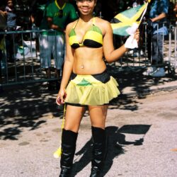 Woman in Jamaican costume waving flag at parade