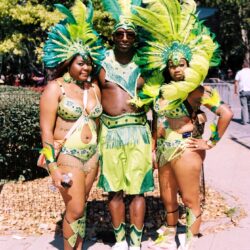 Three carnival performers in green feathered costumes