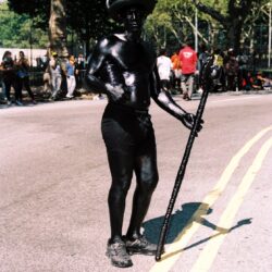 Person in black body paint wearing top hat