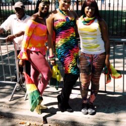 Three people in colorful outfits holding pride flags