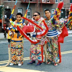 Three men in colorful carnival costumes holding dragon