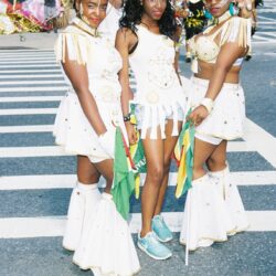 Three women in white carnival costumes holding flags