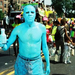 Shirtless man painted blue holding bottle at parade