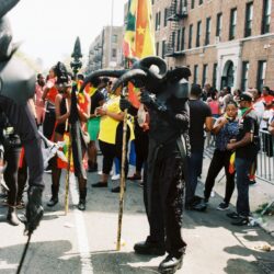 Parade participant wearing elephant mask, holding staff