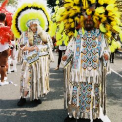 Two parade participants in elaborate yellow feathered headdresses