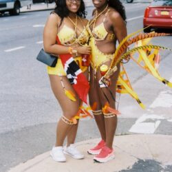 Two women in yellow carnival costumes on sidewalk