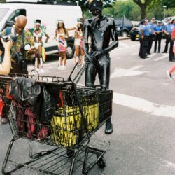 Masked person in black suit pushing shopping cart