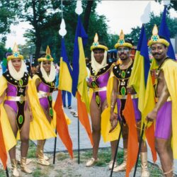 Six performers in purple and yellow carnival costumes