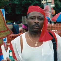 Man wearing red headscarf holding decorated bell
