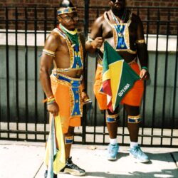 Two men wearing Guyana carnival costumes holding flag