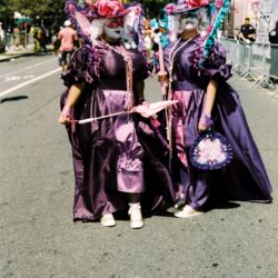 Two masked performers in purple Victorian costumes