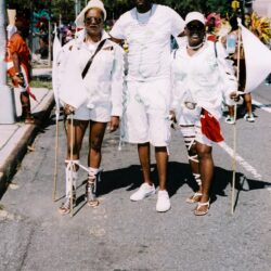 Three people in white parade costumes on street