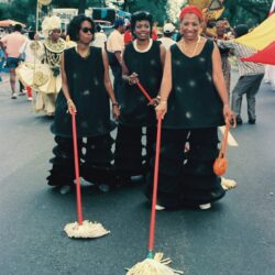 Three women in black parade costumes holding mops