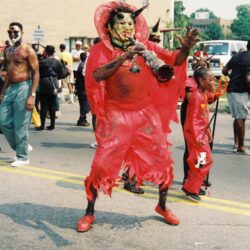Parade performer in red horned costume playing trumpet
