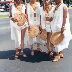 Four women in white costumes with woven fans