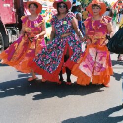 Three women in colorful dresses marching in parade