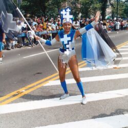 Parade performer in blue cross costume waving