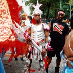 Man in silver carnival costume holding ornate staff