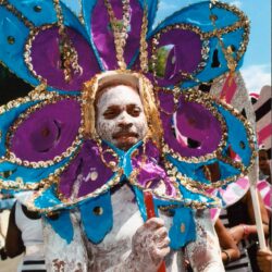 Parade participant in white body paint, flower headdress