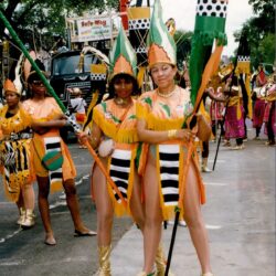 Two women in orange carnival costumes holding flags