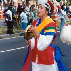Person in colorful traditional outfit playing handheld gong