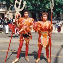 Two performers in red gold costumes holding tridents