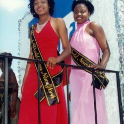 Two women in gowns wearing sashes and tiaras