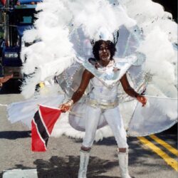 Carnival dancer in white feathers holding Trinidad flag
