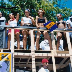 Women dancing on outdoor platform with Barbados flag