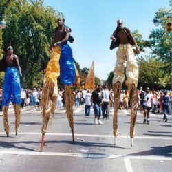 Three stilt walkers in colorful pants at parade
