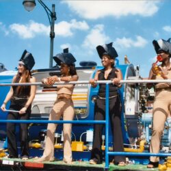 Four women wearing helmets on parade float