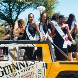Women with sashes on yellow Guinness parade vehicle