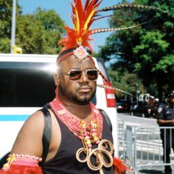 Person wearing feathered carnival headdress and sunglasses