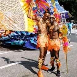 Two men in orange carnival costumes with feathers