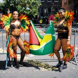 Two women in vibrant carnival costumes, Caribbean flag