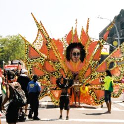 Parade participant wearing large orange sun costume