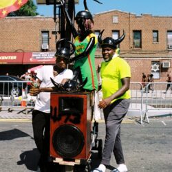 Carnival performers with horns, speaker, Grenada flag