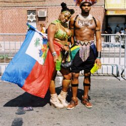 Two people in carnival costumes holding Haitian flag