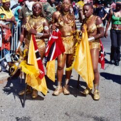 Three women in gold carnival costumes holding flags
