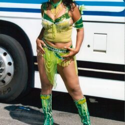 Carnival dancer in green costume by bus