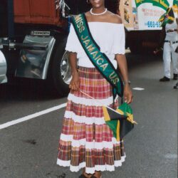 Woman in sash and plaid skirt holding flag