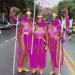 Three women in pink carnival costumes with staffs
