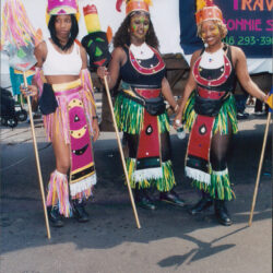 Three women in bright carnival costumes holding staffs
