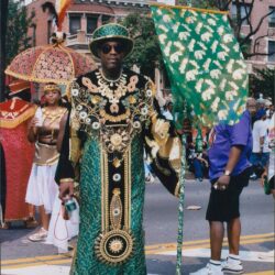 Man in ornate costume holding decorative flag.