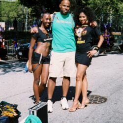 Three people posing outdoors on sunny day.
