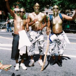 Three men with gold body paint posing outdoors.