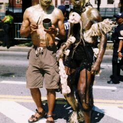 Two men in gold body paint, outdoors.